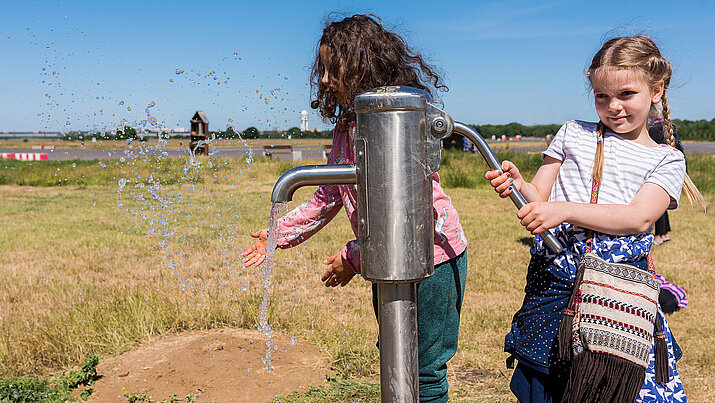 Ein Kind betätigt eine Wasserpumpe auf dem Tempelhofer Feld