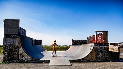 Ein Mann mit gelbem T-Shirt und kurzer gelber Hose fährt mit einem Skateboard in einer Half-Pipe auf dem Tempelhofer Feld